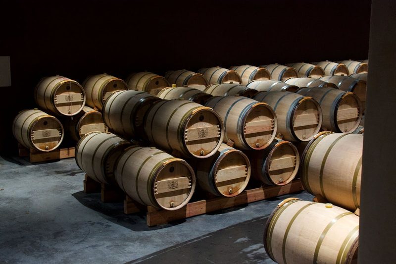 Stacked oak wine barrels in a dimly lit cellar in Pauillac, France