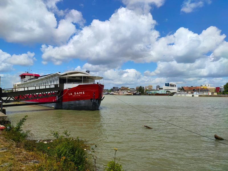 A vibrant red boat docked on the Garonne River with Bordeaux urban waterfront in the background