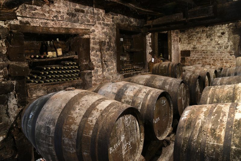 Wine cellar with wooden barrels and dusty bottles stacked against old stone walls