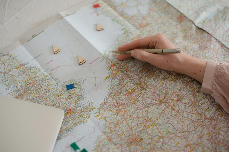 Hand holding a pen over a map of Europe while planning a travel route