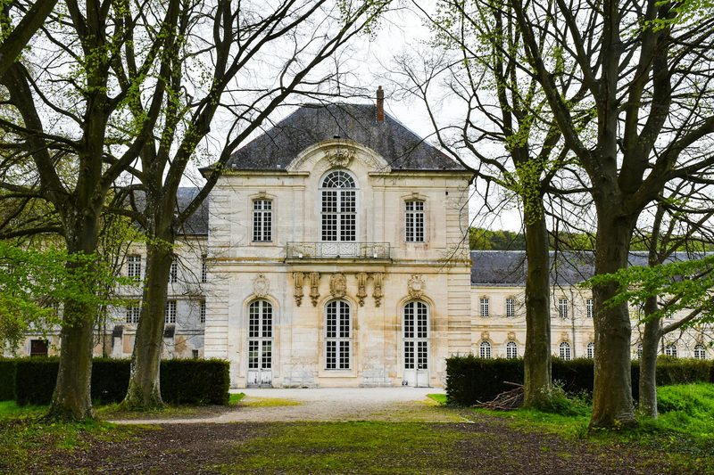 An elegant historic French mansion with classical architecture surrounded by mature trees