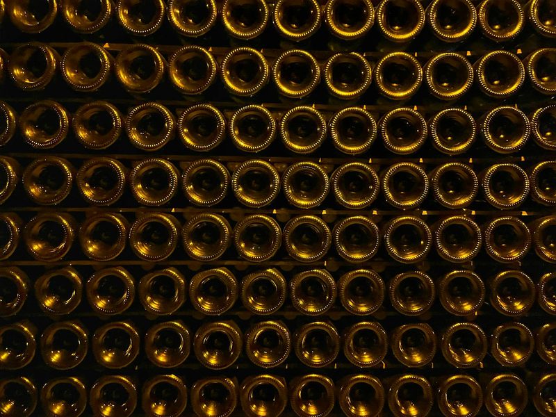 Rows of stacked champagne bottles in a dimly lit underground cellar with warm tones