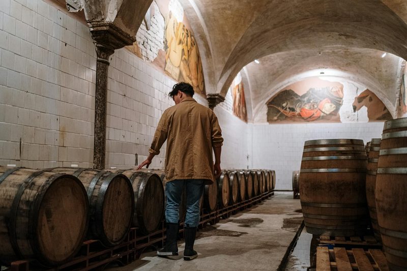 A man inspecting wooden barrels in a wine cellar, checking on the aging process during a cellar tour