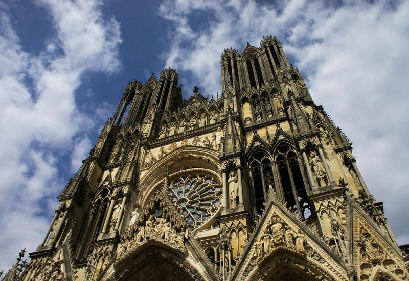 The Gothic facade of Reims Cathedral, where French kings were crowned, set against a clear blue sky