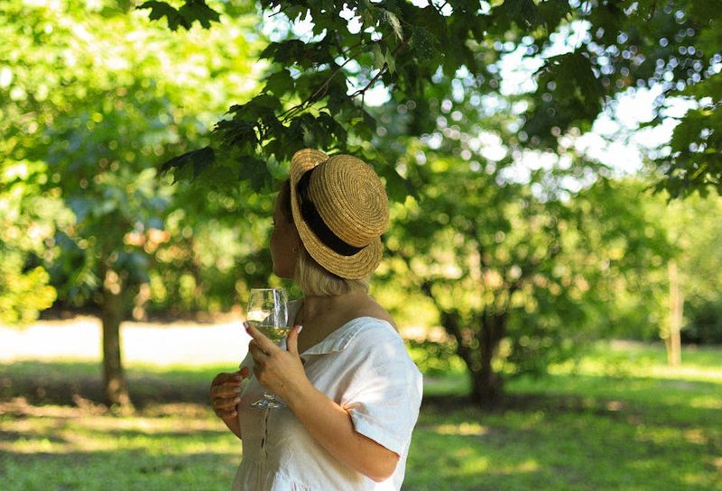 Woman in a straw hat holding a wine glass enjoying sunshine in a vineyard
