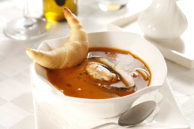 Rich tomato seafood soup with mussels served with a croissant