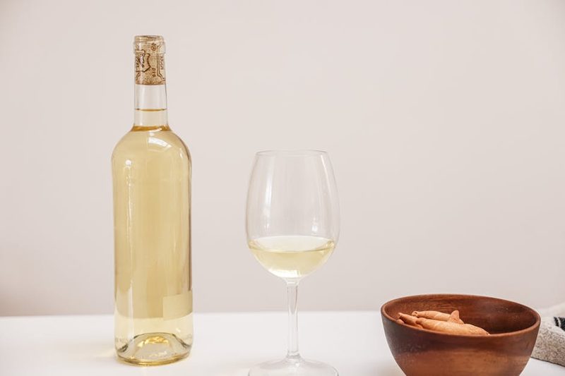 Bottle and glass of white wine alongside a wooden bowl on an outdoor table
